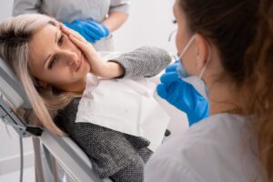 Patient holding side of face in pain while lying back in dentist's chair.